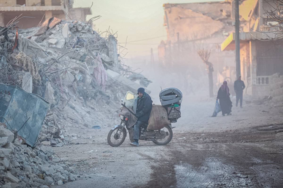 A Syrian man with his belongings rides a bicycle through the collapsed buildings as Syrians continue their lives in harsh conditions in quake hit Jindires district of Aleppo, Syria after 7.7 and 7.6 magnitude earthquakes hit multiple provinces of Turkiye and Syria on February 17, 2023. [Muhammed Said - Anadolu Agency]