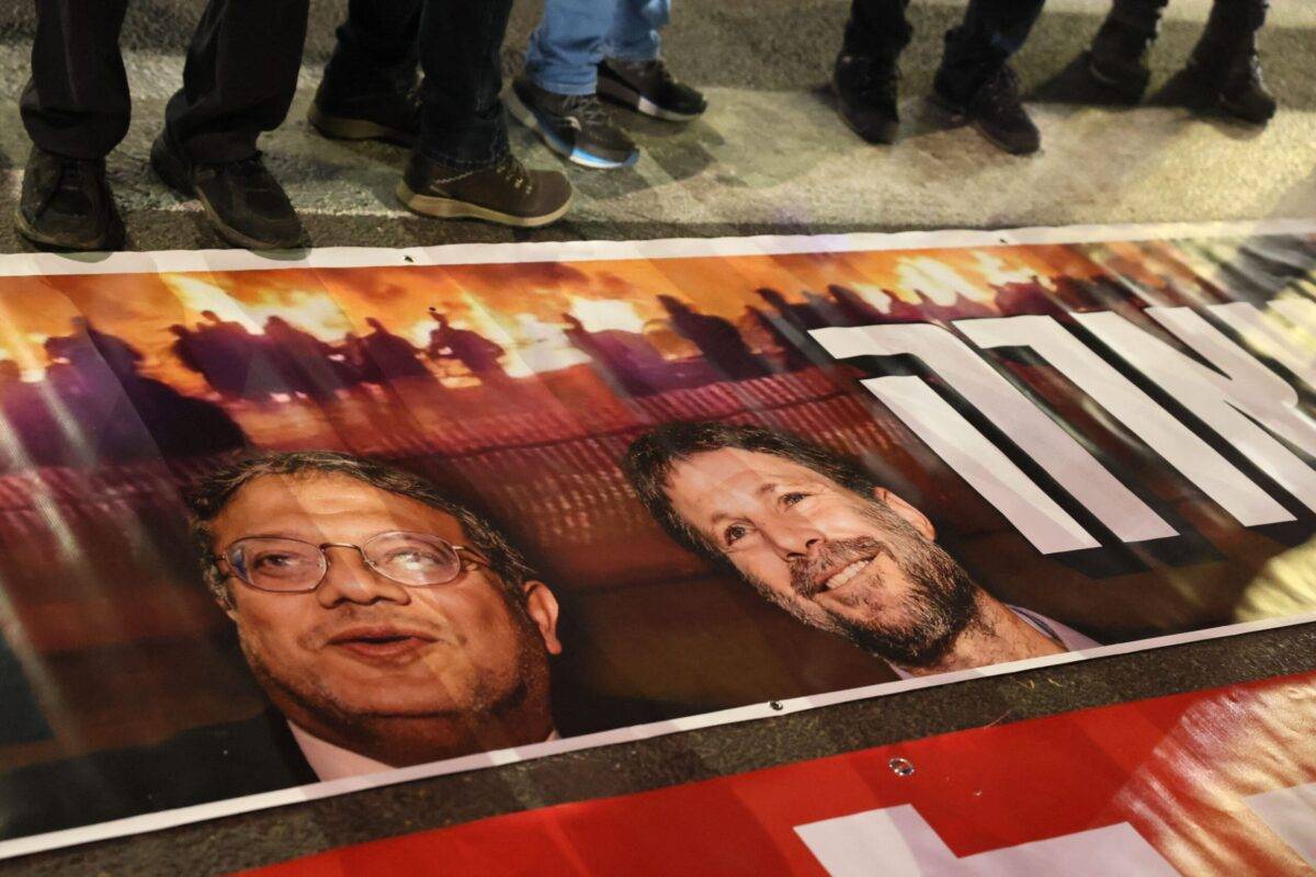 Israelis stand next to a poster with the portraits of Minister of National Security Itamar Ben-Gvir and Finance Minister Bezalel Smotrich on March 4, 2023 [JACK GUEZ/AFP via Getty Images]