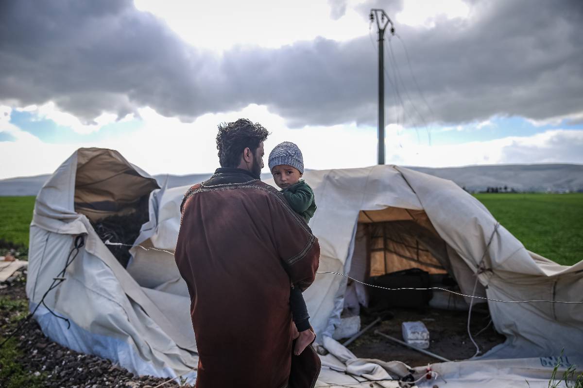A man holding his child is seen in front of a damaged tent as windstorm becomes effective for 2 days and hit 32 thousand civilians in 60 refugee camps for displaced people and 11 temporary shelter for earthquake survivors in Idlib, Syria on March 29, 2023 [Muhammed Said - Anadolu Agency]