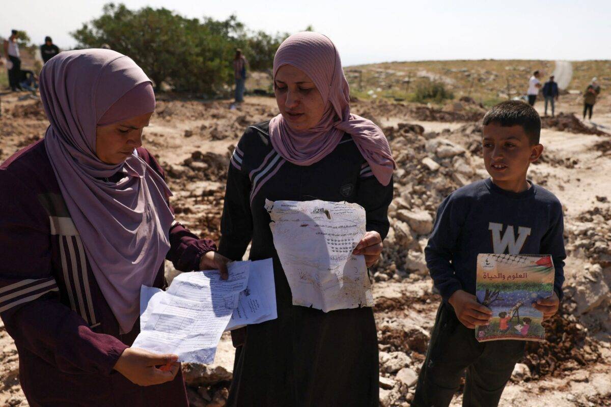 Palestinians pick up papers and books from the site of a school that was demolished by the Israeli authorities who said it was built without permission in the village of Jabbet al-Dhib, east of Bethlehem in the occupied West Bank, on May 7, 2023 [HAZEM BADER/AFP via Getty Images]