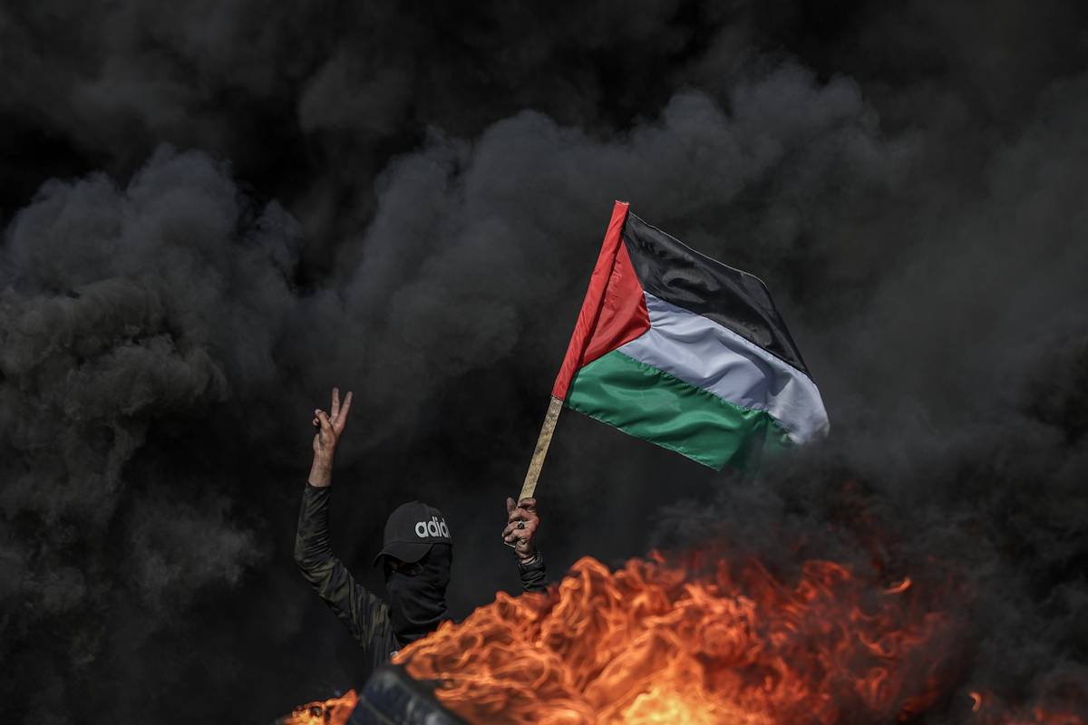 Gazaian people holding the Palestine flag set tyre on fire to stage a protest against killing Palestinians by Israeli forces, in Gaza Strip on June 19, 2023 [Ali Jadallah - Anadolu Agency]