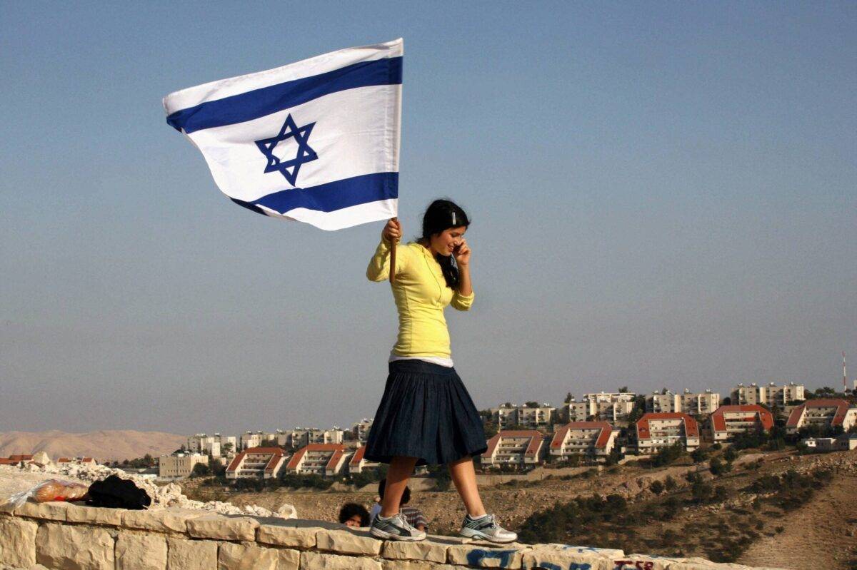 Back dropped by the West Bank settlement of Maale Adumim, an Israeli right-wing activist holds the national flag [GALI TIBBON/AFP via Getty Images]