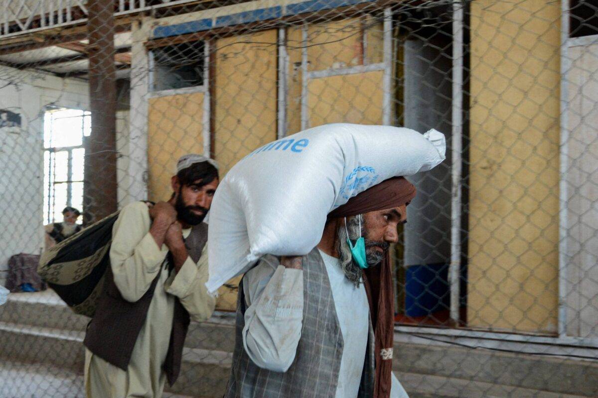 Afghan men carry sacks of grains they received at a World Food Programme (WFP) facility as an aid to Afghan people with children suffering from malnourishment in Kandahar on April 21, 2022 [JAVED TANVEER/AFP via Getty Images]