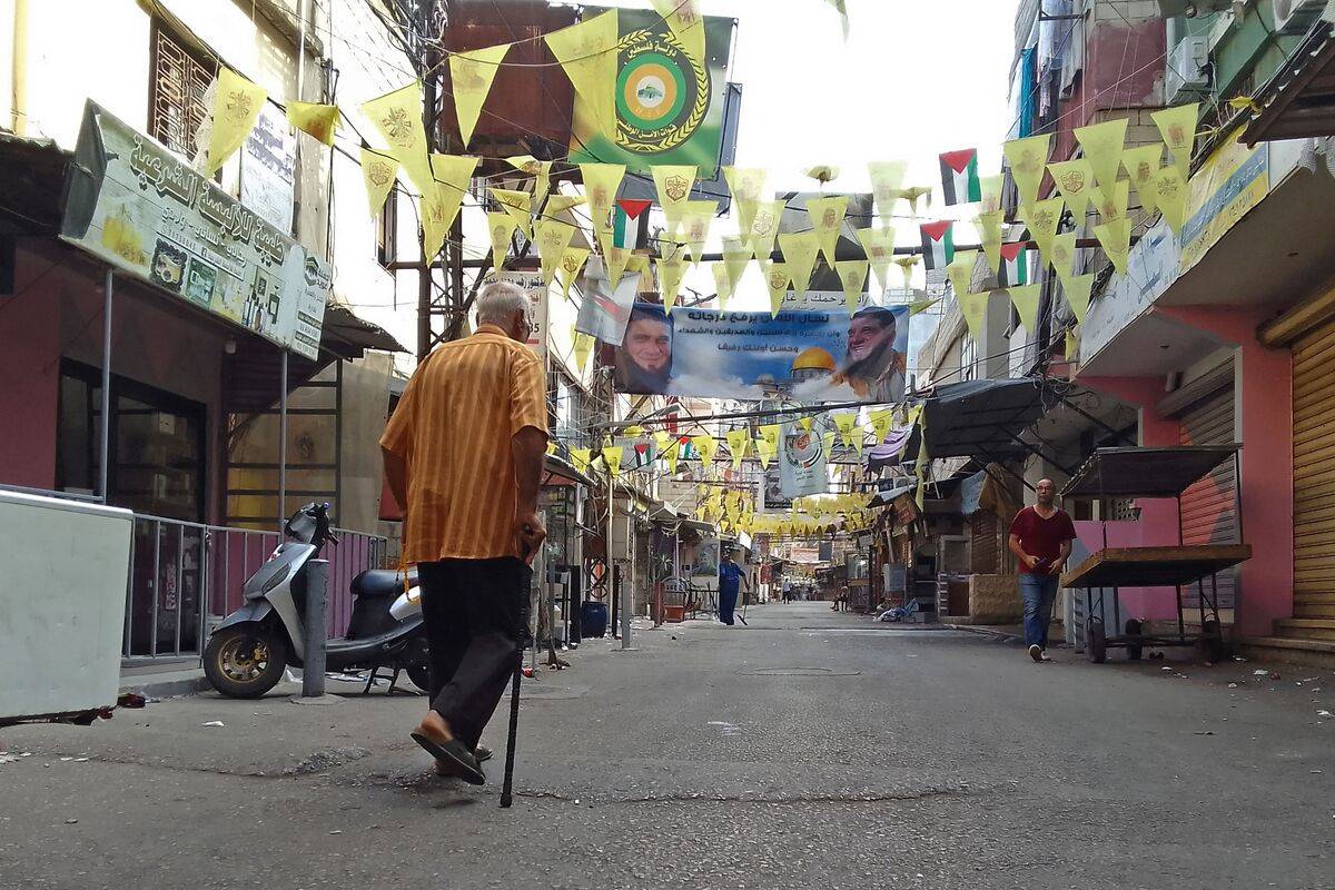 People walk past closed shops in the aftermath of clashes between the Fatah movement and Islamists inside the Ain el-Helweh Palestinian refugee camp in the southern coastal city of Sidon on August 1, 2023. [Photo by MAHMOUD ZAYYAT/AFP via Getty Images]