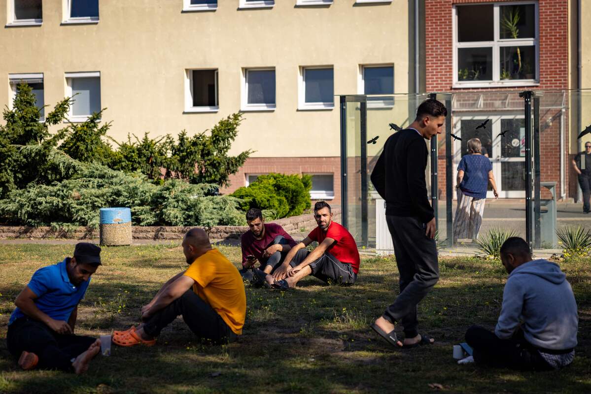Residents sit on the lawn in the courtyard between housing blocks at Brandenburg's Central Immigration Authority (ZABH) center, housing some 1400 asylum seekers in Eisenhuttenstadt, eastern Germany, on September 28, 2023. [Photo by ODD ANDERSEN/AFP via Getty Images]