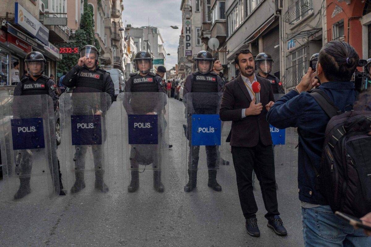 A journalist works on live coverage afar from demonsrators as Turkish riot police block journalists to shoot a press release in front of a pro-Kurdish Peoples' Democracy Party (HDP) office, at Beyoglu district in Istanbul on October 2, 2023 [BULENT KILIC/AFP via Getty Images]