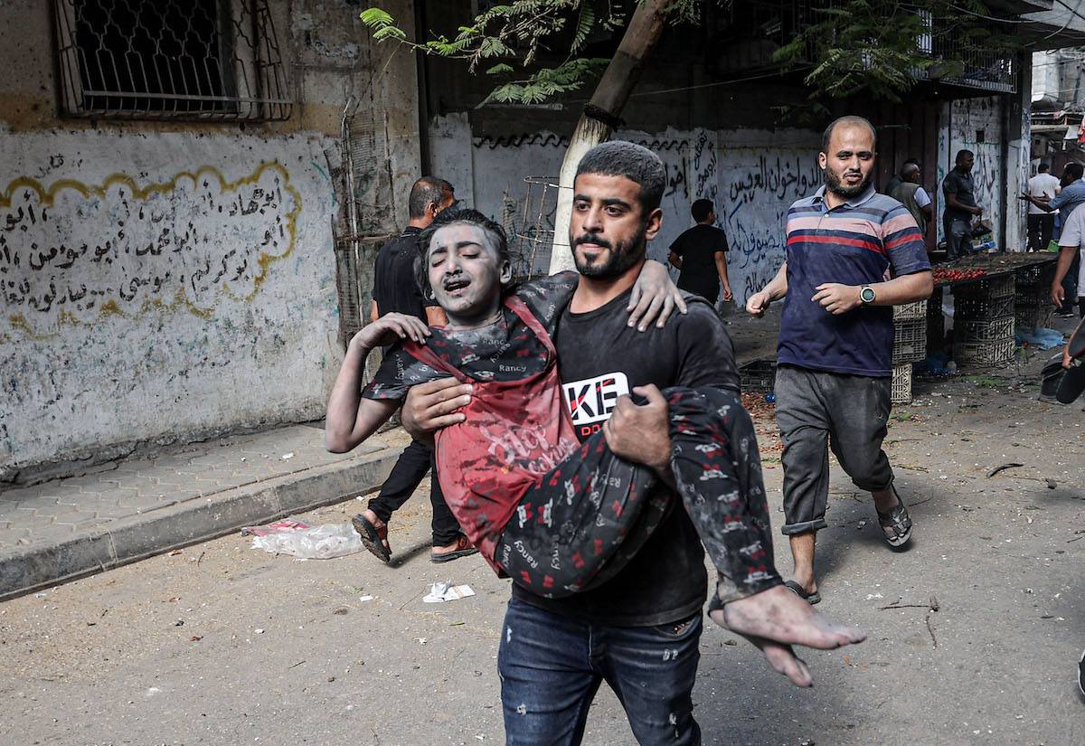 An injured Palestinian child covered in blood and dust being taken to a hospital amid destruction caused by Israeli airstrikes on Bureij refugee camp in central Gaza Strip on November 02, 2023 [Mustafa Hassona - Anadolu Agency]