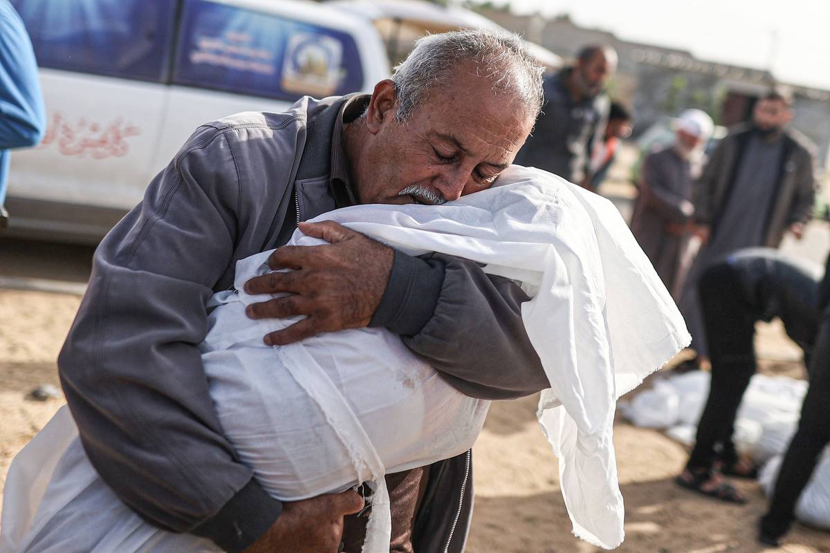 A man hugs the lifeless body of a child as the Palestinians killed in Israeli attacks are taken out of the mortuary of Al-Aqsa Martyr's Hospital for burial in Deir al Balah, Gaza on November 22, 2023 [Mustafa Hassona - Anadolu Agency]