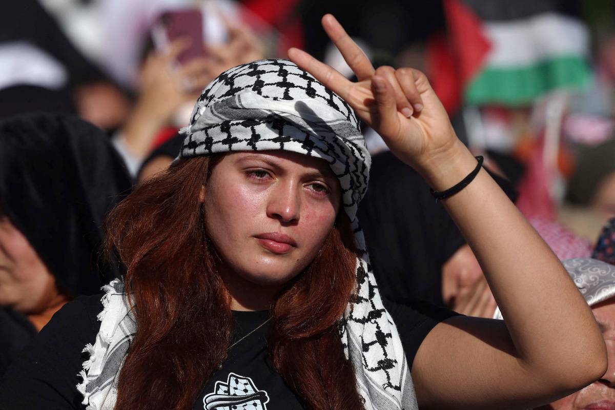 A woman wearing a chequerred black and white keffiyeh flashes the V-sign for victory during a protest in Rabat on December 10, 2023 in solidarity with the Palestinians amid Israel's relentless bombardment of the Gaza Strip [FADEL SENNA / AFP Via Getty Images]
