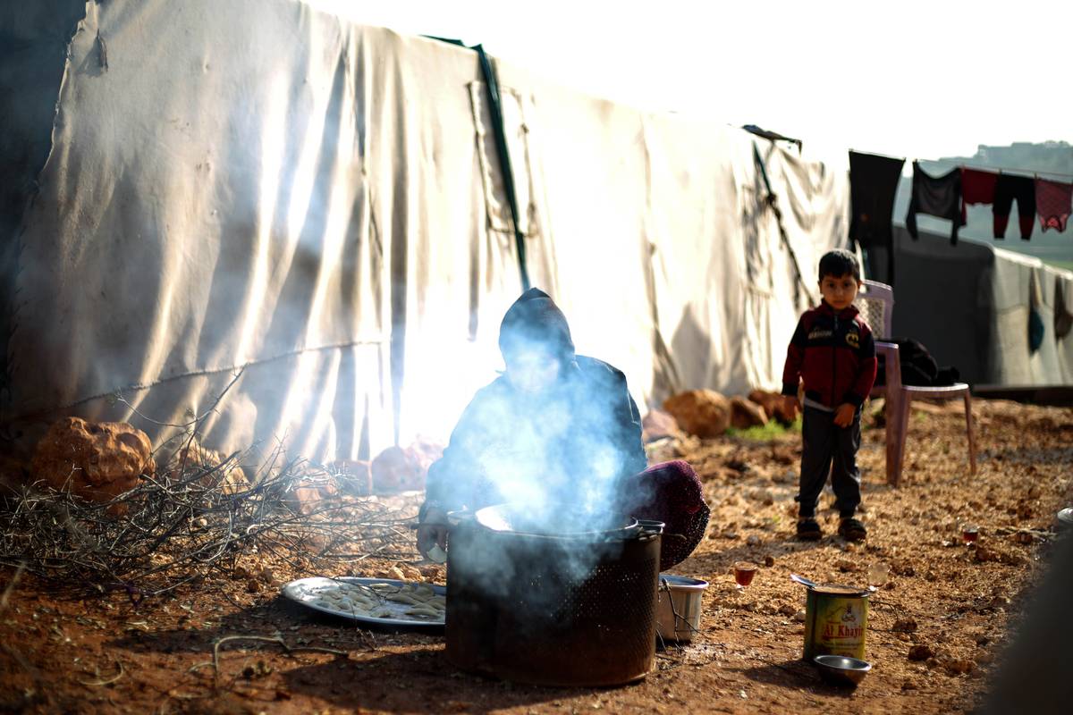 A Syrian child, who has to struggle with hard life conditions and cold winter as a refugee in Bettin Camp, watches a man cooking in Idlib, Syria on January 20, 2024. [İzettin Kasım - Anadolu Agency]