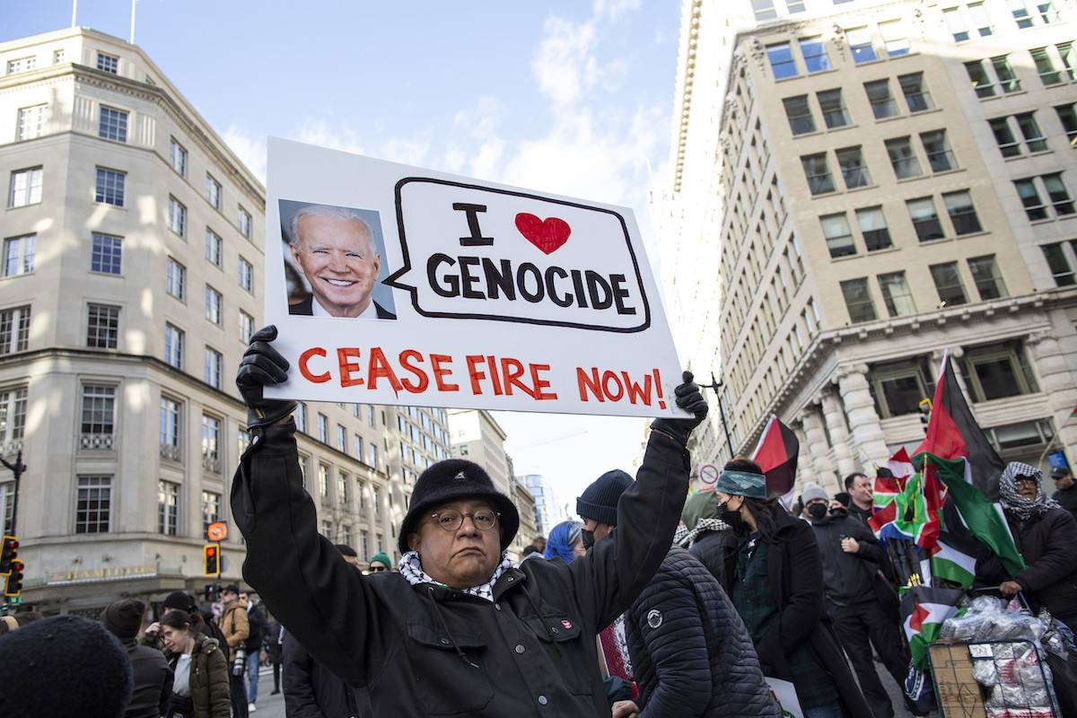 A demonstrator holding a sign with President Joe Biden picture and the text reading “I Love Genocide, Ceasefire Now” as he joins in demonstration, in Washington, DC, on 13 January 2024 [Probal Rashid/LightRocket via Getty Images]