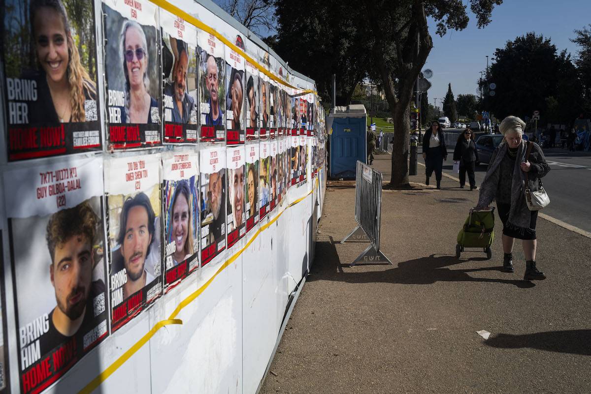 People walk past posters on a wall bearing portraits of Israeli hostages held in Gaza near the parliament in Jerusalem on January 22, 2024. [JEWEL SAMAD/AFP via Getty Images]