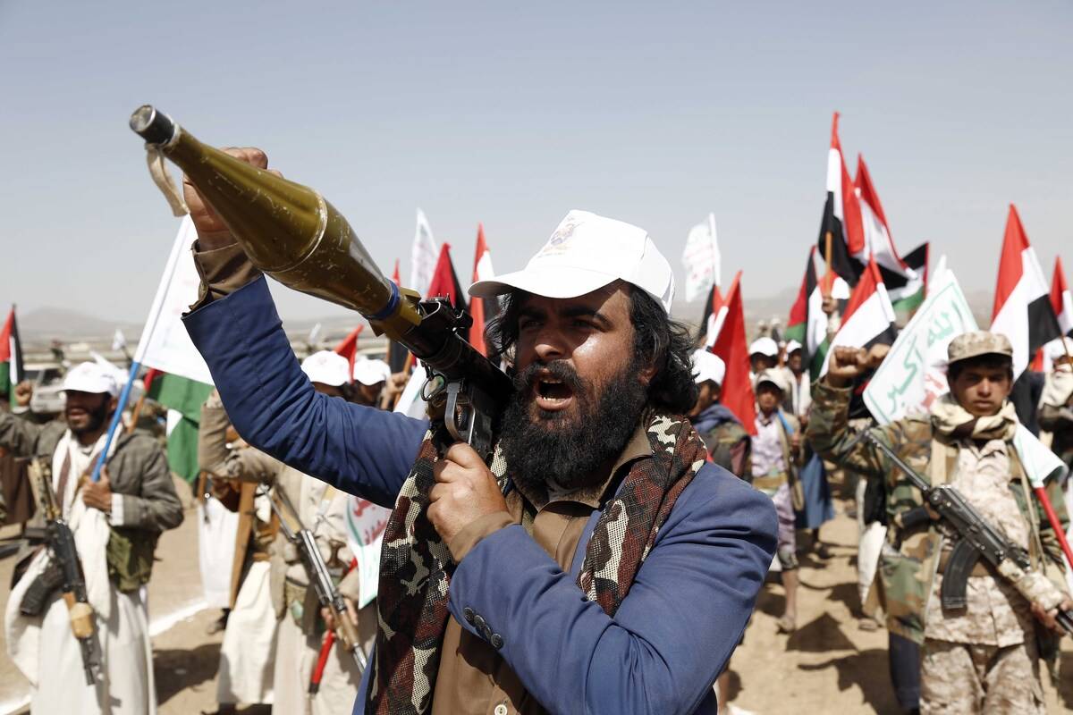 A man carries a weapon as people attend a graduation ceremony for cadet, completed their military training under the name of "Aqsa Flood", organized by the Houthis, in Arhab district of Sana'a, Yemen on February 4, 2024. [Mohammed Hamoud - Anadolu Agency]