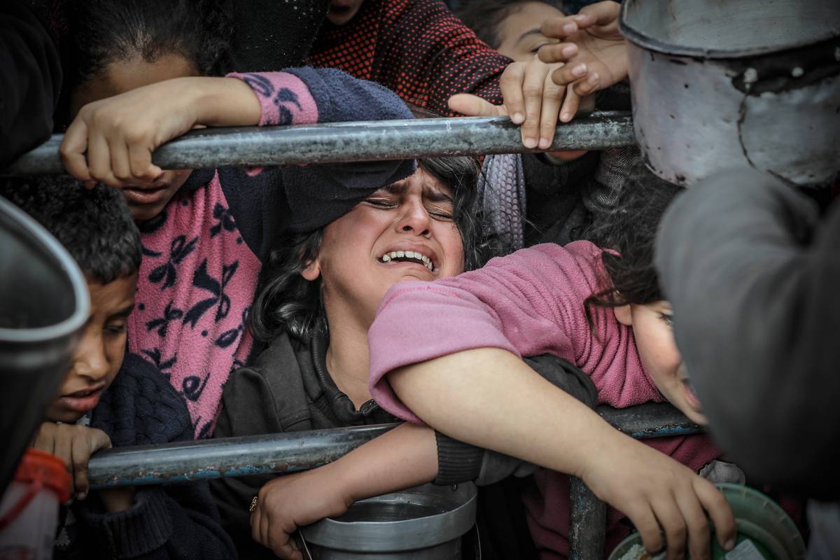 Palestinian child gestures as crying amid Palestinian children wait in line to receive food prepared by volunteers for Palestinian families ,displaced to Southern Gaza due to Israeli attacks, between rubbles of destroyed buildings in Rafah, Gaza on February 10, 2024. [Belal Khaled - Anadolu Agency ]
