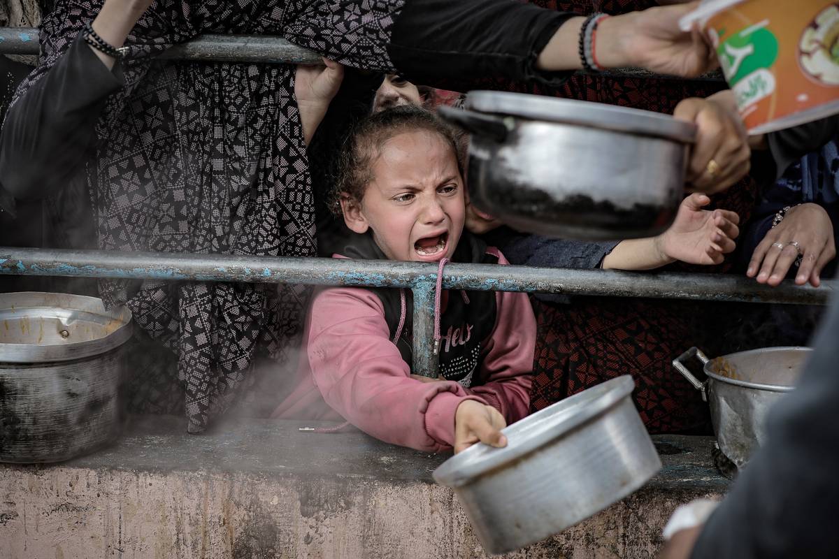 Palestinian children wait in line to receive food prepared by volunteers for Palestinian families ,displaced to Southern Gaza due to Israeli attacks, between rubbles of destroyed buildings in Rafah, Gaza on February 10, 2024. [Belal Khaled - Anadolu Agency]