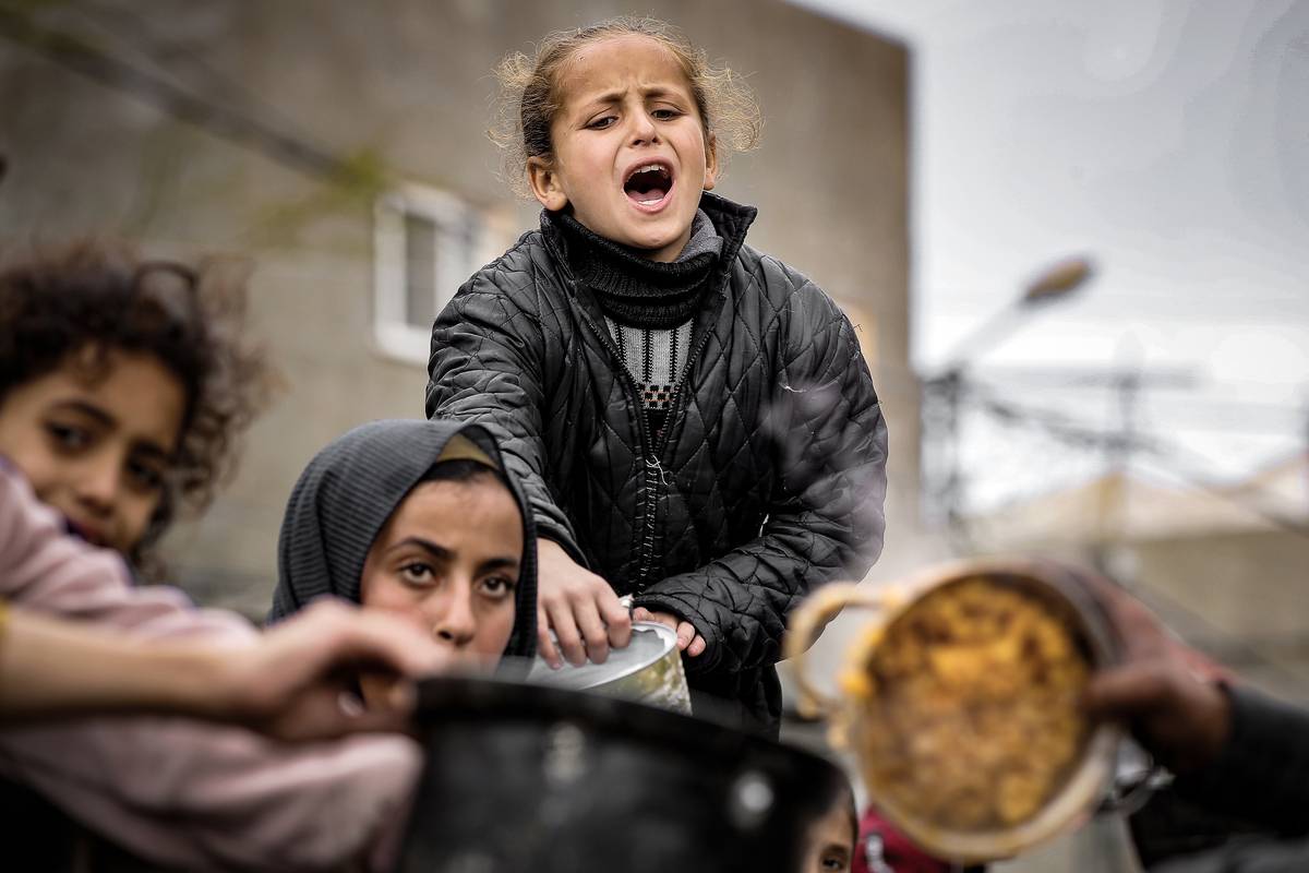 Palestinian children wait in line to receive food prepared by volunteers for Palestinian families ,displaced to Southern Gaza due to Israeli attacks, between rubbles of destroyed buildings in Rafah, Gaza on February 10, 2024. [Belal Khaled - Anadolu Agency]