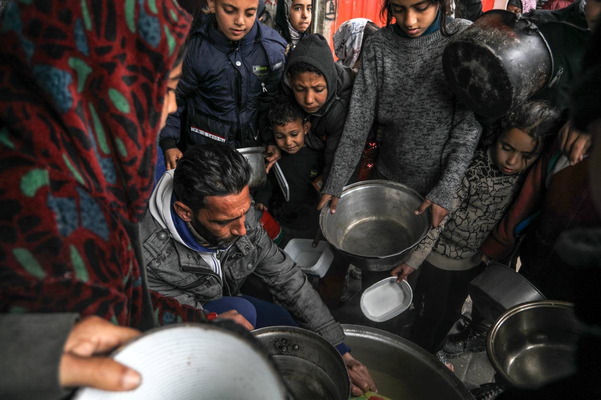 Palestinians holding empty bowls receive food distributed by volunteers of charities as people facing hunger crisis and famine risk due to the Israeli embargo imposed on the territory, in Rafah, Gaza on February 18, 2024. [Abed Rahim Khatib - Anadolu Agency]