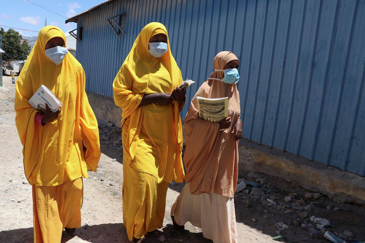 Students walk in a Mogadishu neighbourhood wearing face masks. [Photo by ABDIRAZAK HUSSEIN FARAH/AFP via Getty Images]