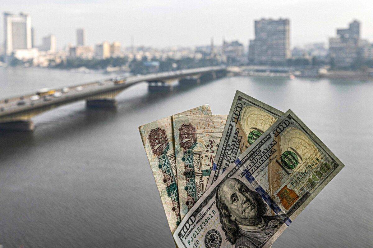 Two pairs of US hundred dollar and Egyptian hundred pound notes are held before a window showing the skyline of Egypt's capital Cairo and the Nile river on January 16, 2023 [KHALED DESOUKI/AFP via Getty Images]