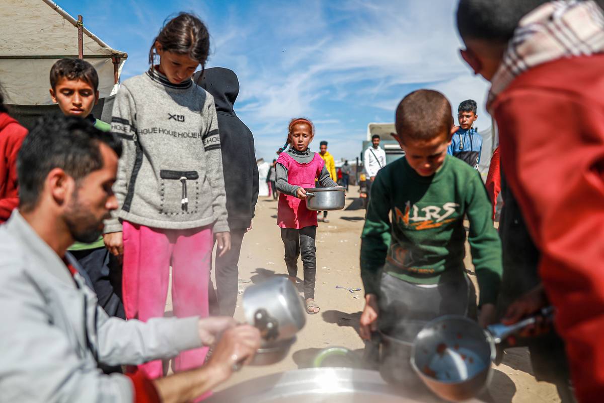 Palestinian children get food to the bowls makeshift tent set up near the border of Egypt as Israeli attacks continue in Rafah, Gaza on March 08, 2024. Jehad Alshrafi - Anadolu Agency]
