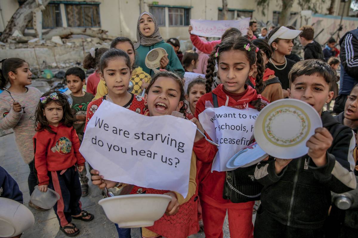 Palestinian children holding banners and empty bowls, gather to protest the food shortages in the city due to Israeli attacks and demanding a ceasefire in Gaza City, Gaza on March 12, 2024. [Omar Qattaa - Anadolu Agency]