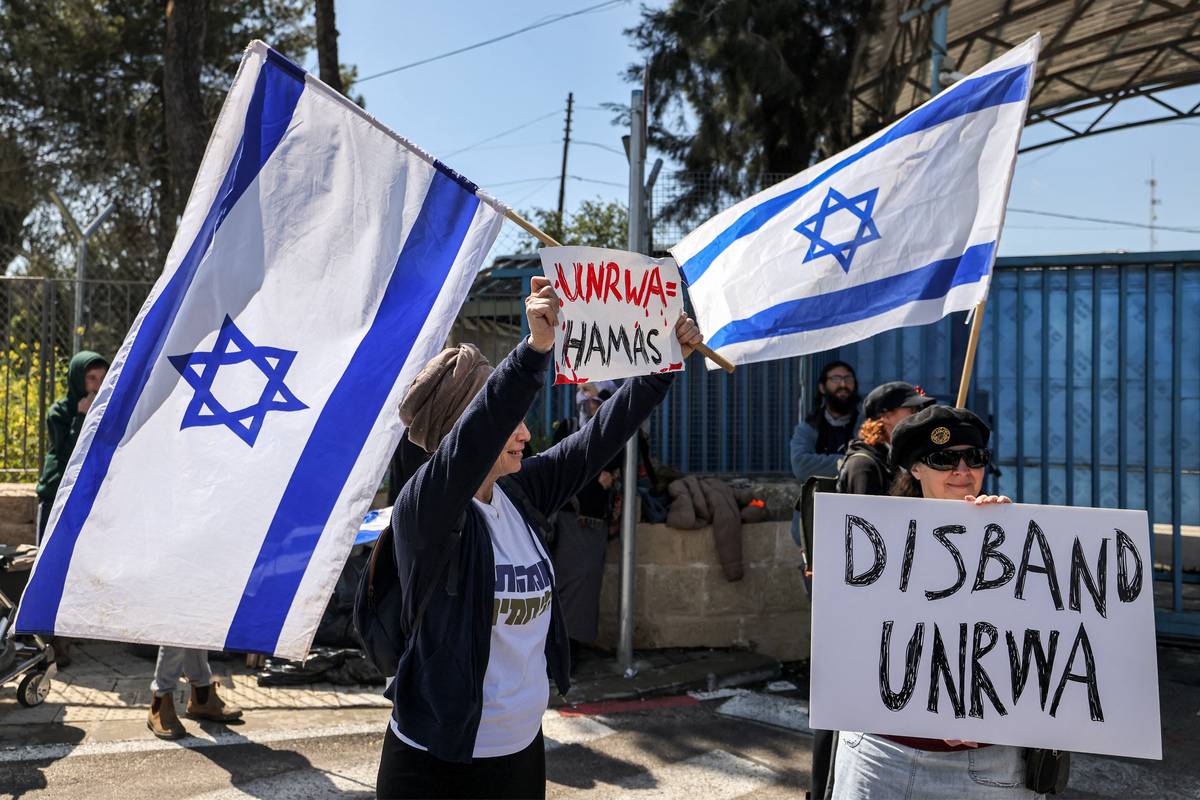 A right-wing Israeli protester holds an Israeli flag and a sign while standing with others gathering outside the West Bank field office of the United Nations Relief and Works Agency for Palestine Refugees (UNRWA) in Jerusalem on March 20, 2024. [Photo by AHMAD GHARABLI/AFP via Getty Images]