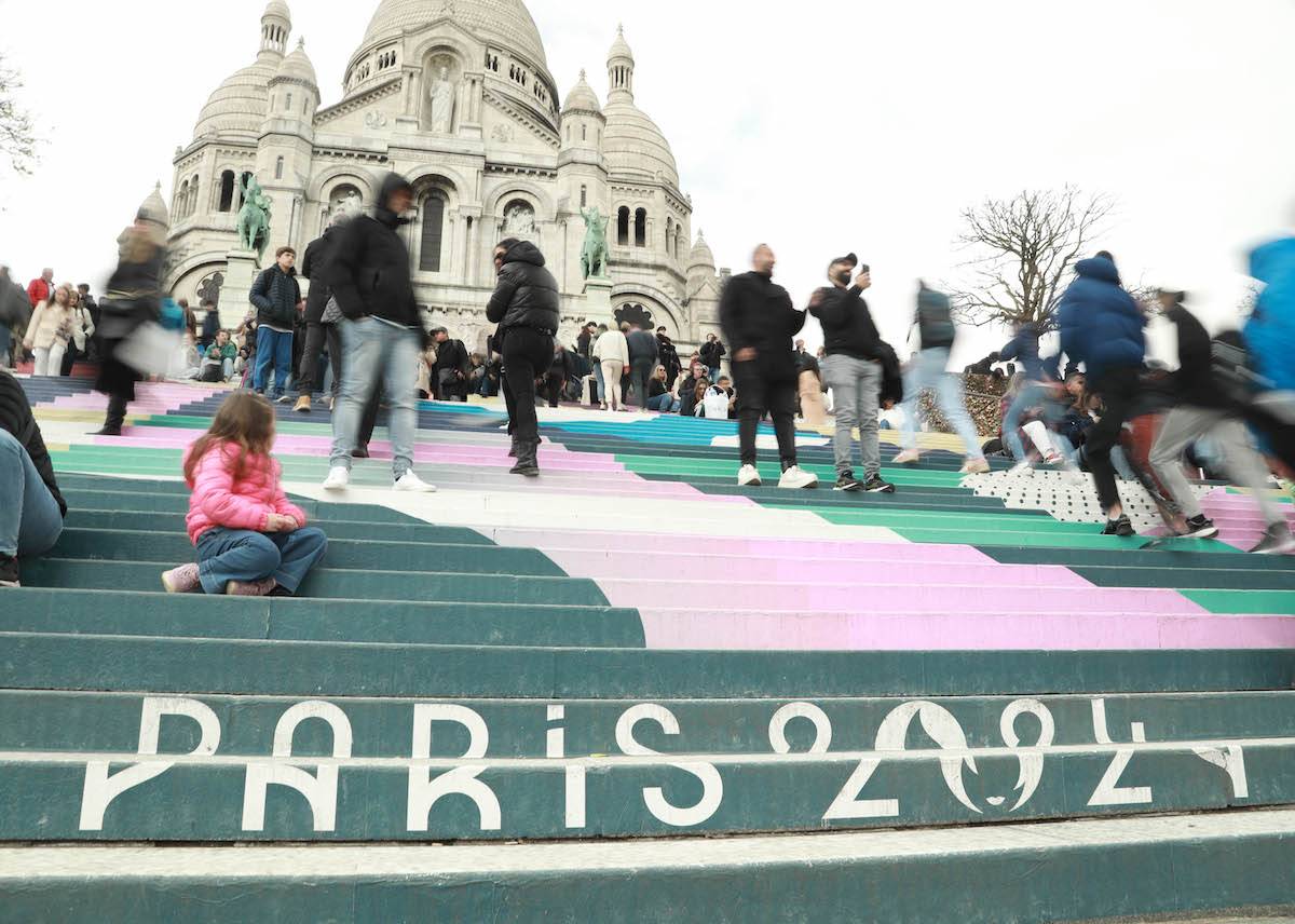 People walk on the stairs painted in the colors of the upcoming Paris 2024 Olympics in front of the Sacre-Coeur Basilica on top of the Montmartre hill on April 22, 2024 in Paris, France. [Mohamad Salaheldin Abdelg Alsayed - Anadolu Agency]