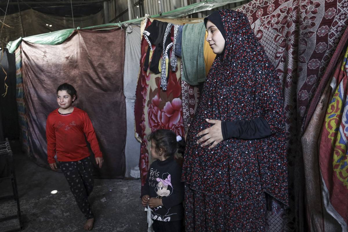 A pregnant Palestinian woman (R) displaced from northern Gaza stands in a warehouse where she is taking shelter in Rafah, in the southern Gaza Strip, on February 29, 2024. [Photo by -/AFP via Getty Images]