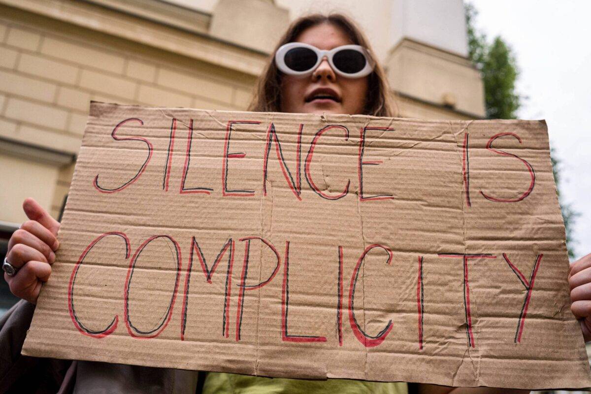 A protester holds a placard that says "Silence is Complicity" during demonstration in Poland On 7 June 2024 [Neil Milton/SOPA Images/LightRocket via Getty Images]