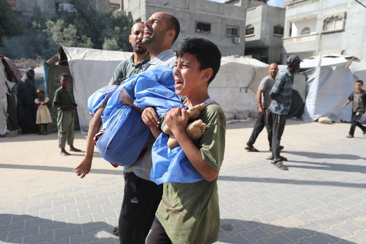 A Palestinian man carries the bloody body of a child to Al Awda Hospital after the Israeli attack that hit a water refill point belonging to displaced Palestinians in the “New Camp” area northwest of Nuseirat Camp, killing 10 people, including 6 children, in Gaza City, Gaza on July 13, 2025. [Moiz Salhi - Anadolu Agency]