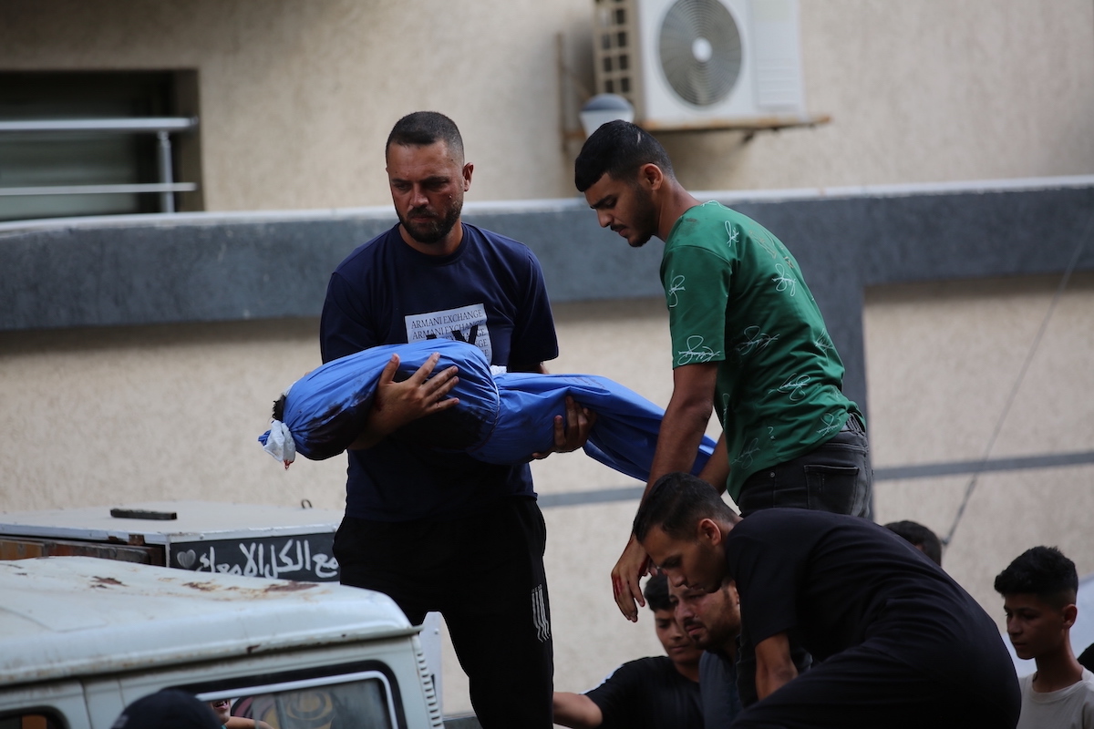 A grieving man carries the shrouded bodies of victims outside Al-Awda Hospital in Nuseirat, Gaza, after an Israeli airstrike targets a residential area in the refugee camp on July 29, 2025. [Hassan Jedi - Anadolu Agency]
