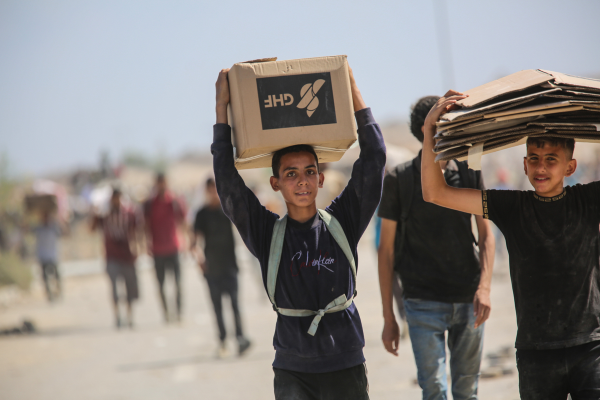 A Palestinian boy carries food supplies as residents flock to the Netzarim Corridor to receive limited aid, with hunger deepening across Gaza amid ongoing Israeli attacks and blockade, on August 4, 2025. [Hassan Jedi - Anadolu Agency]