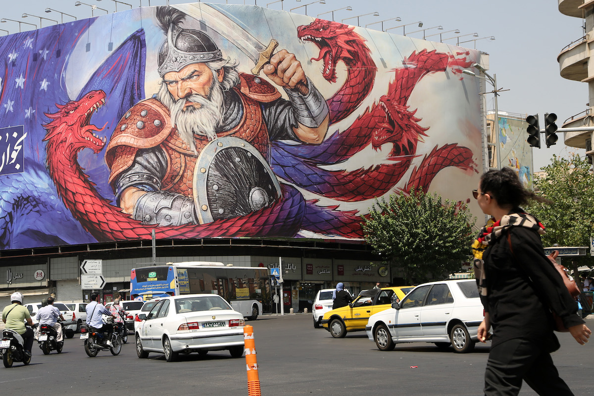 A giant banner depicting Iran’s mythological hero Rostam fighting a dragon symbolizing the United States is put up in Azadi Square, while Iranian citizens are walking through the street in Tehran, Iran on August 18, 2025. [Fatemeh Bahrami - Anadolu Agency]