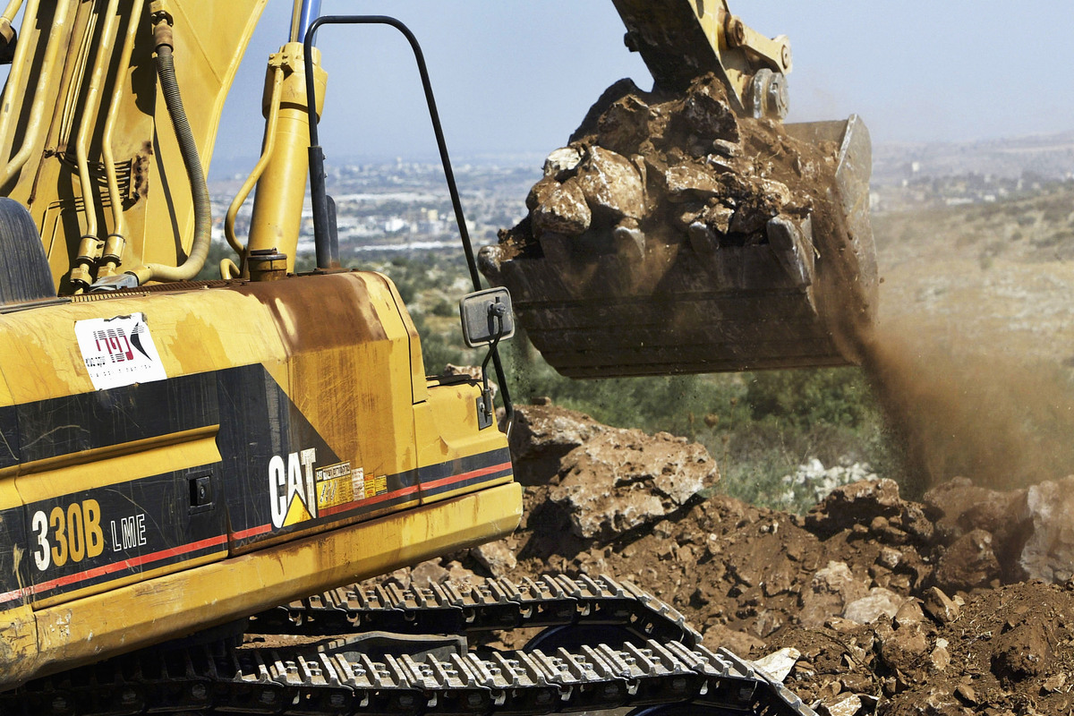 An Israeli contractor's Caterpillar 330B LME hydraulic excavator grabs a load of soil and rocks as it clears the path of Israel's separation fence on Palestinian land July 1, 2004 in the West Bank village of Az-Zawiya. [Photo by David Silverman/Getty Images]