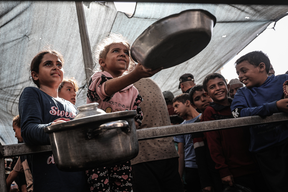 Palestinians, including children, wait with pots to receive hot meals distributed by charity organizations, as people struggle with hunger due to the Israeli food blockade at Nuseirat refugee camp in Gaza City, Gaza on October 21, 2025. [Moiz Salhi - Anadolu Agency]
