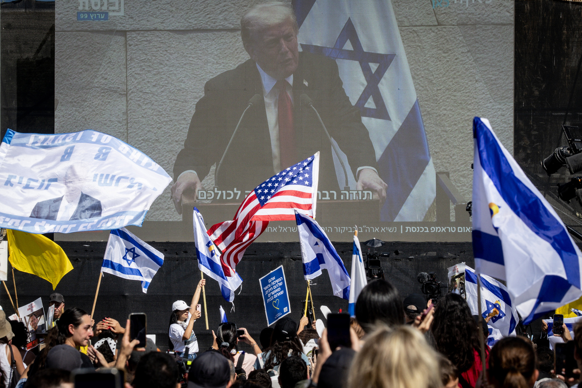 People watch U.S. President Donald Trump address the Knesset, Israel's parliament, on a giant screen in Hostages Square on October 13, 2025 in Tel Aviv, Israel. [Photo by Chris McGrath/Getty Images]