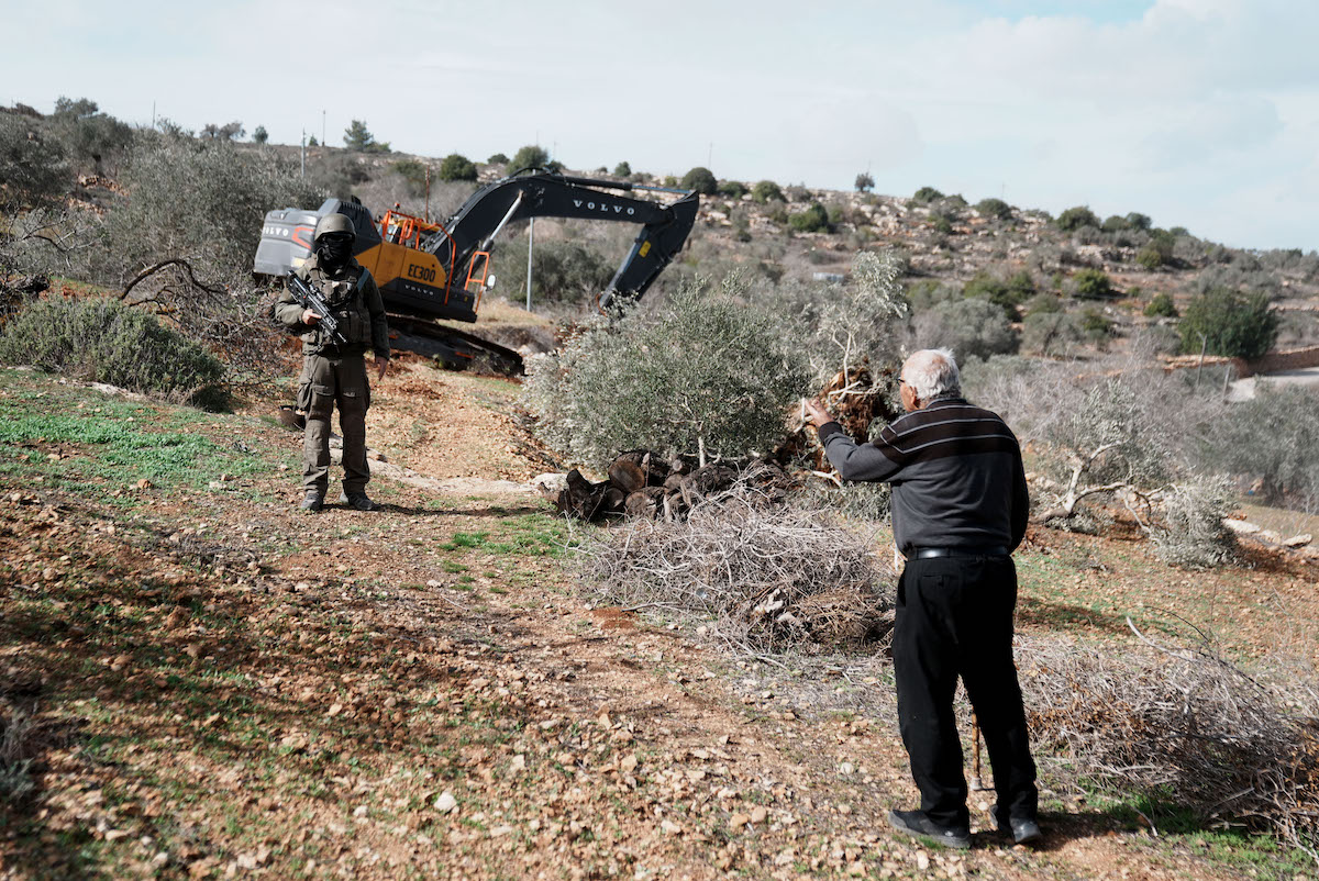 Israeli soldiers stand by as Israeli construction vehicles destroy agricultural lands and uproot centuries-old olive trees in the village of Karyut, south of the city of Nablus, West Bank on December 08, 2025. [Issam Rimawi - Anadolu Agency]