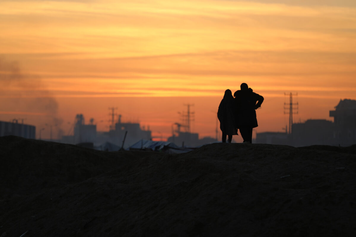 The silhouettes of two Palestinians are seen as Palestinians living in the Nuseirat refugee camp continue their daily lives under difficult conditions amidst the rubble left behind by Israeli attacks in Deir al-Balah, Gaza on December 22, 2025. [Adem Bilal - Anadolu Agency]